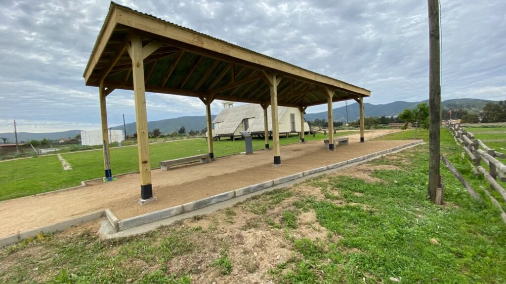 Vista lateral del nuevo sombreadero de madera, con cubierta metálica y pilares sobre apoyos de hormigón, en el Sitio de Memoria Melinka-Puchuncaví.